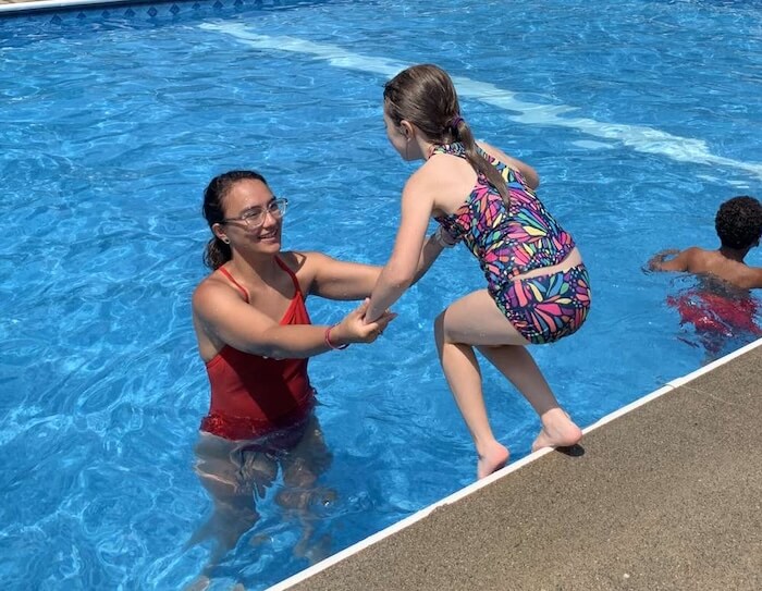 A lifeguard helping a girl jump into a pool